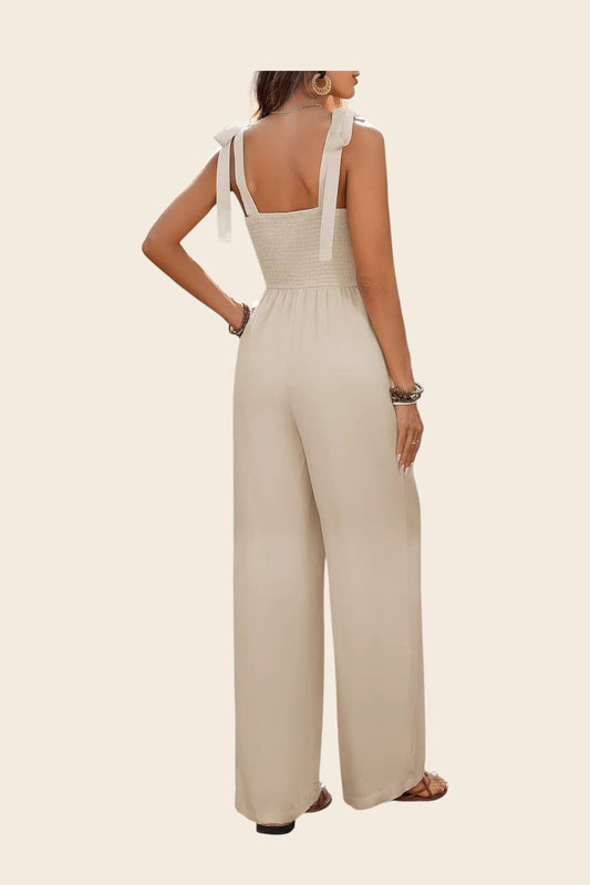 Combinaison beige en viscose fluide, taille haute, jambes larges, avec un haut smocké et bretelles à nœuds. Maison de la combi.