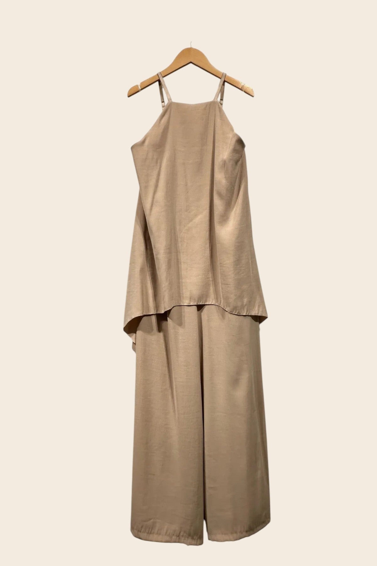 Combinaison fluide beige présentée sur cintre, bretelles fines ajustables, décolleté rond, buste évasé effet cape retombant sur un pantalon large palazzo