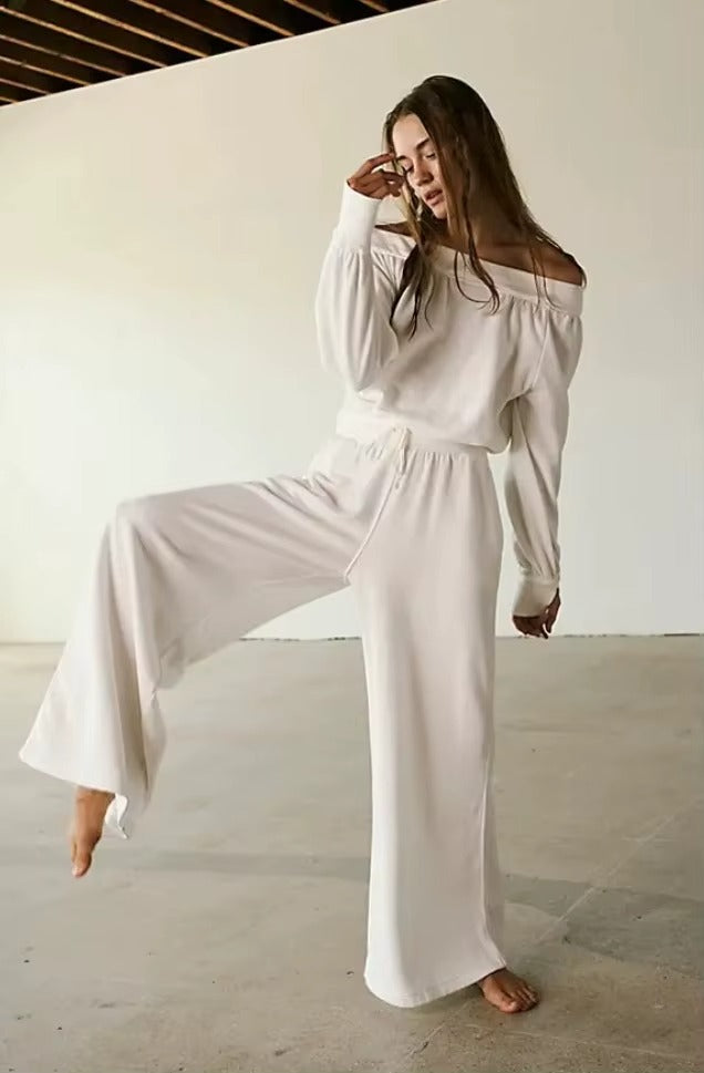 Une combinaison pour femme , de type pantalon, de couleur blanche, avec coupe large, epaules dénudées, la femme se tient sur une jambe