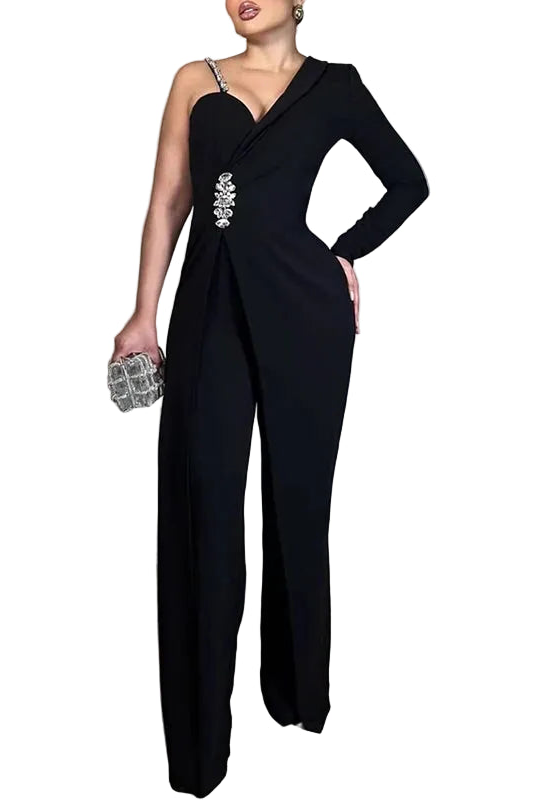 Combinaison noire asymétrique soirée portée de face avec bretelle en strass, col blazer et broche bijou à la taille.