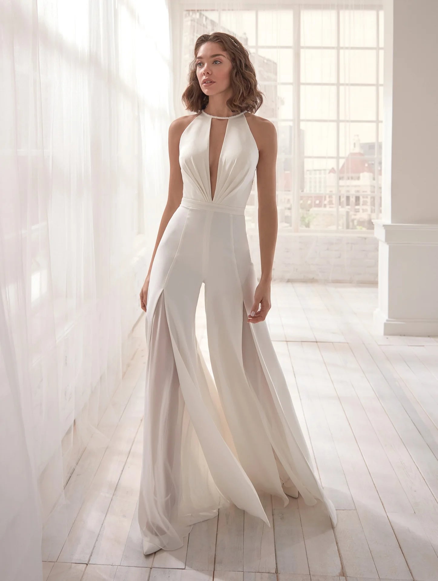 Combinaison blanche chic portée debout dans un salon blanc lumineux mettant en valeur sa coupe élancée et moderne.