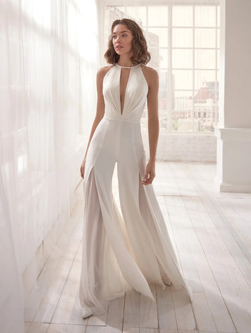Combinaison blanche chic portée debout dans un salon blanc lumineux mettant en valeur sa coupe élancée et moderne.